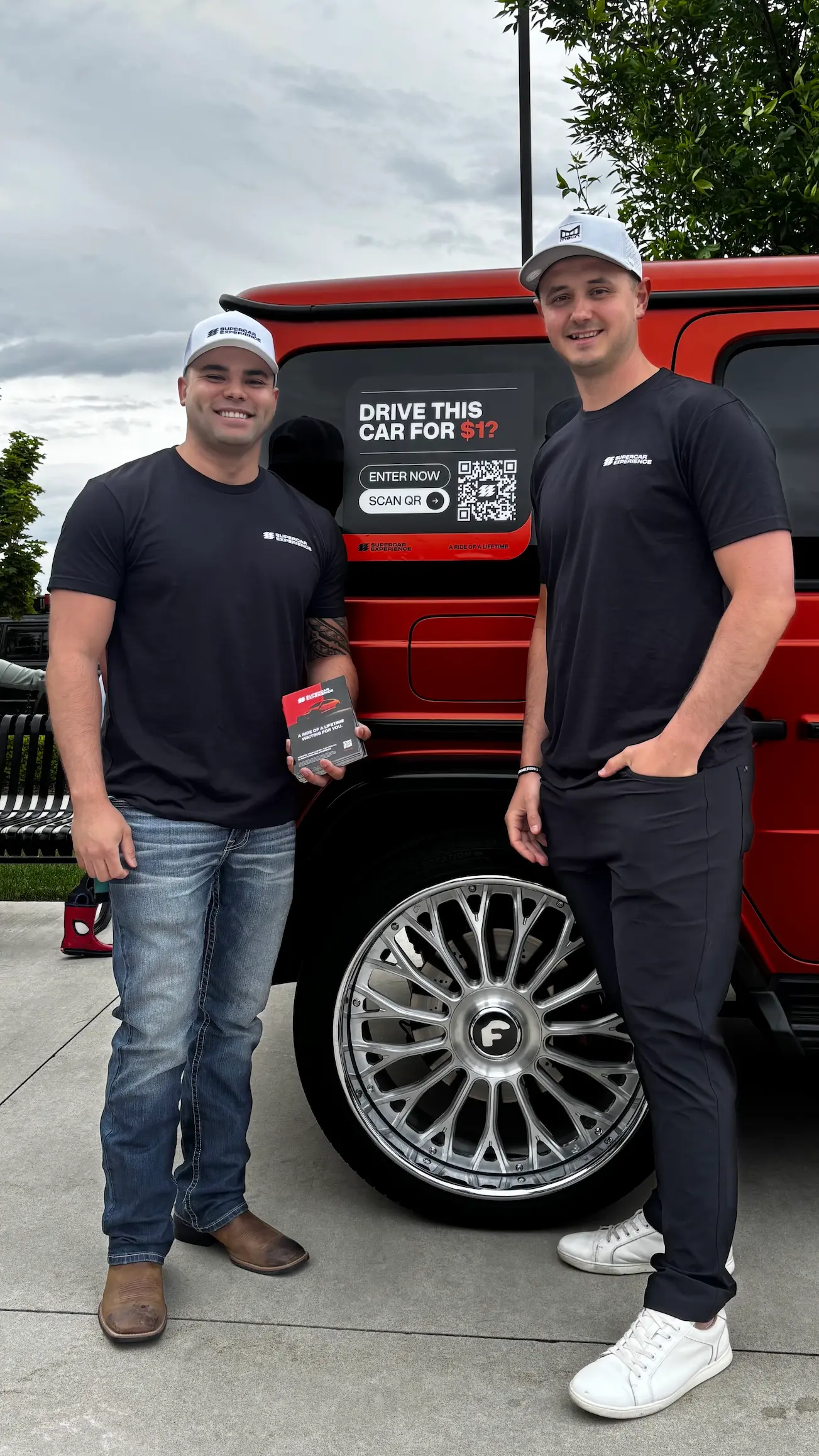 Supercar Experience team members holding a key card beside a red SUV